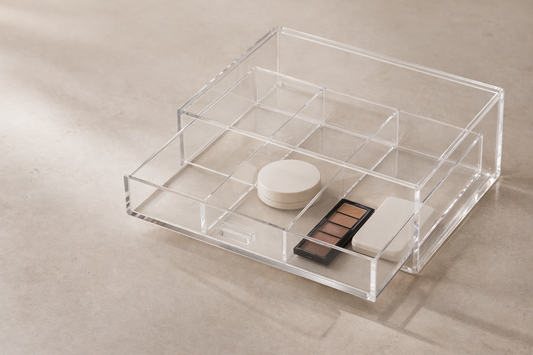 Clear acrylic vanity drawer organizer with flat items arranged in a single layer and one empty space, creating a minimal setup that stays easy to access without stacking.