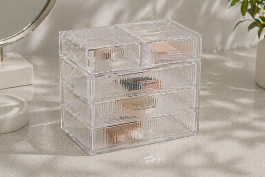 Clear 4-tier drawer organizer with separated compartments organizing makeup items with visible spacing.