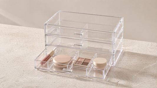 Clear acrylic drawer organizer with items separated into individual compartments and one empty section, preventing mixing and improving organization control.