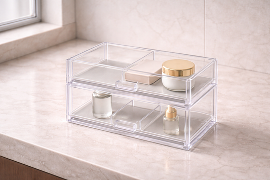 Clear acrylic two-tier drawer organizer with partially empty compartments and 2–3 items spaced apart, showing modular adaptability and expandable storage structure