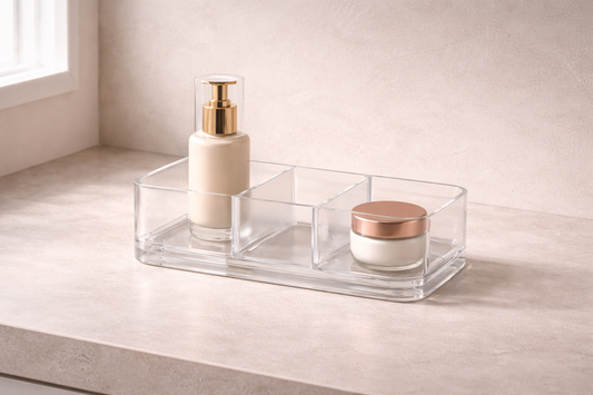 Skincare setup for easier and more consistent routines featuring a clear divided acrylic organizer with a gold-pump bottle and cream jar on a stone countertop