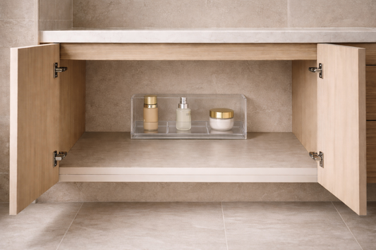 Single acrylic organizer placed deep inside an under-vanity cabinet with three skincare items and large empty foreground space showing hidden storage structure