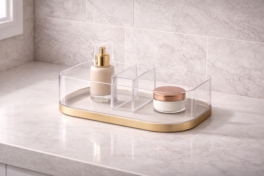 Vanity organization for faster and more streamlined mornings featuring a clear acrylic organizer with a gold base and divided compartments on a marble countertop